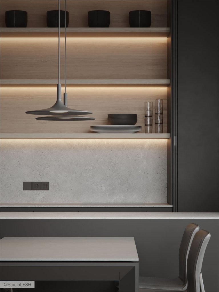 Интерьер современной кухни: темные минималистичные фасады, встроенная техника, подсветка, серый обеденный стол с двумя современными стульями, светлый ламинат на полу.