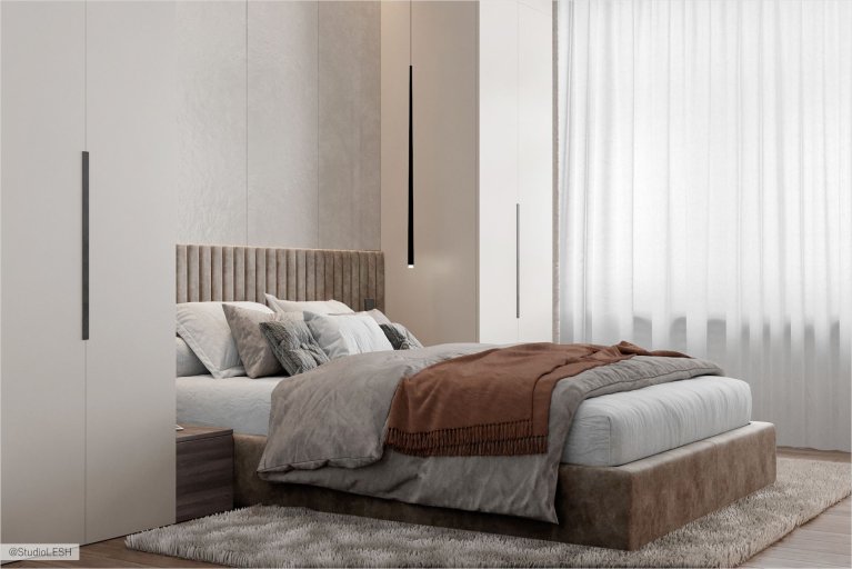 Изображение светлой и уютной спальни с большой кроватью, на которой лежит коричневое одеяло. В комнате есть все необходимое для комфортного проживания: удобная кровать, места для хранения вещей и современный декор