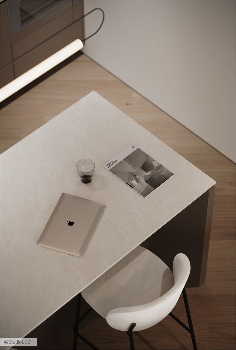 Вид сверху на кухонный остров с ноутбуком, чашкой и журналом. Белые барные стулья стоят рядом. На заднем плане виден кухонный гарнитур с серыми фасадами и длинным светильником
