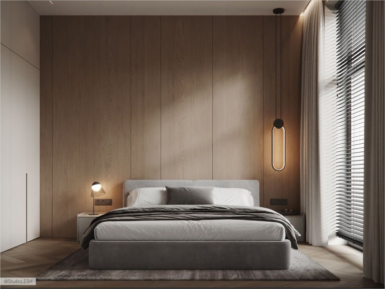 Интерьер спальни в светлых тонах с большой двуспальной кроватью, деревянной стеной за изголовьем, двумя тумбочками по бокам и подвесными светильниками. В комнате также есть большое окно с жалюзи и плотными шторами