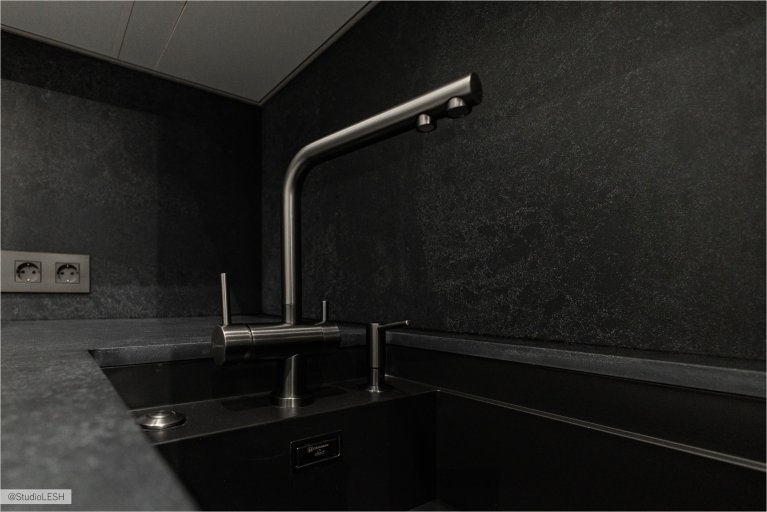 Стильная кухня с черным смесителем с гибким изливом, идеально подходящим для современной кухни. Смеситель установлен на темной столешнице рядом с темной раковиной. Видны также другие элементы кухонного гарнитура, выполненные в едином стиле, и рейлинг с крючками на заднем плане