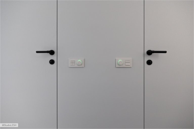 Две белые двери с черными ручками и замками, создающие контраст и привлекающие внимание. Ручки имеют современный дизайн и удобны в использовании. Двери идеально вписываются в минималистический интерьер комнаты, подчеркивая ее стиль и элегантность