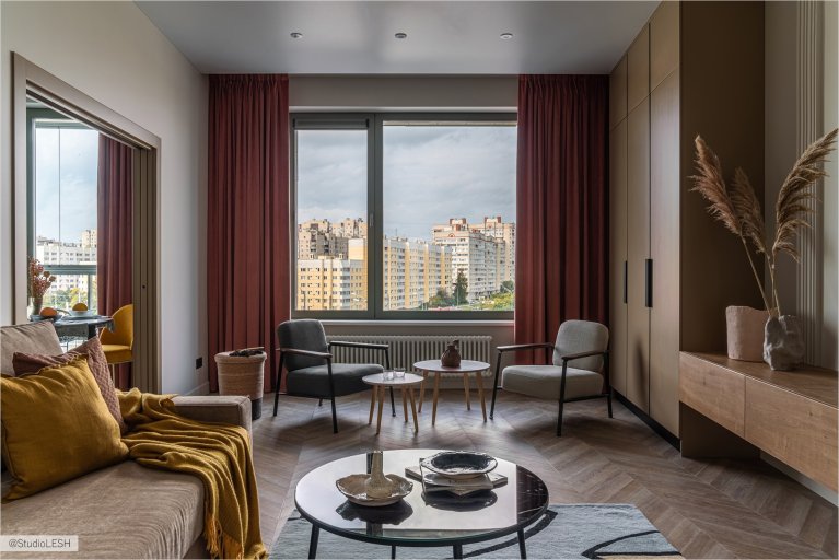 Гостиная с серым диваном, двумя креслами, круглым журнальным столиком и большим окном