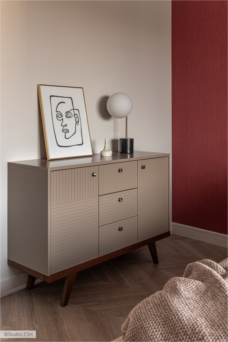 В комнате стоит комод с выдвижными ящиками, выполненный из светлого дерева